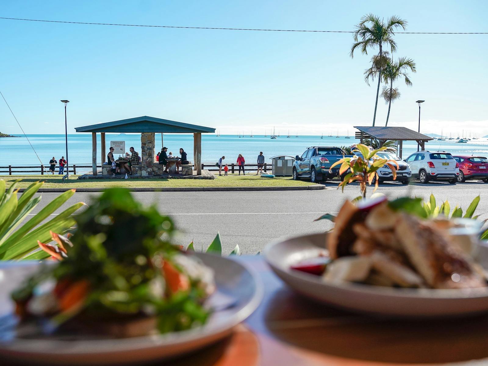 View from a cafe window with food on the table overlooking the ocean and picnic area