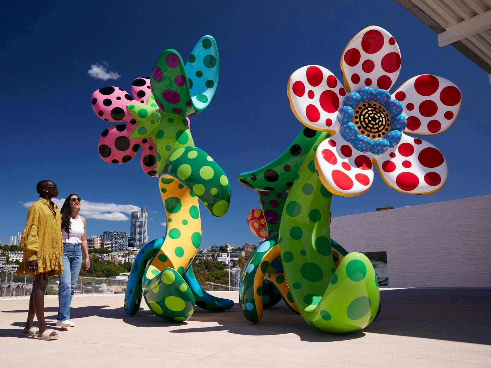 Two women standing in front of two colourful flower-like sculptures filled with dots