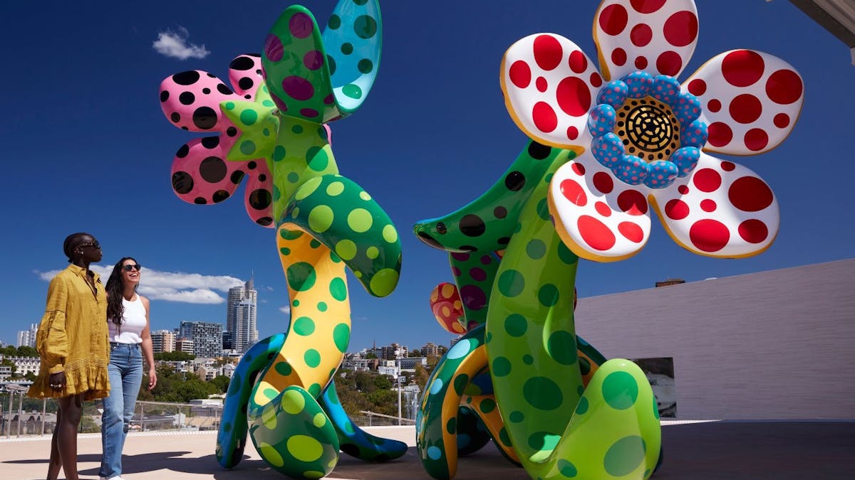 Two women standing in front of two colourful flower-like sculptures filled with dots Two women standing in front of two colourful flower-like sculptures filled with dots