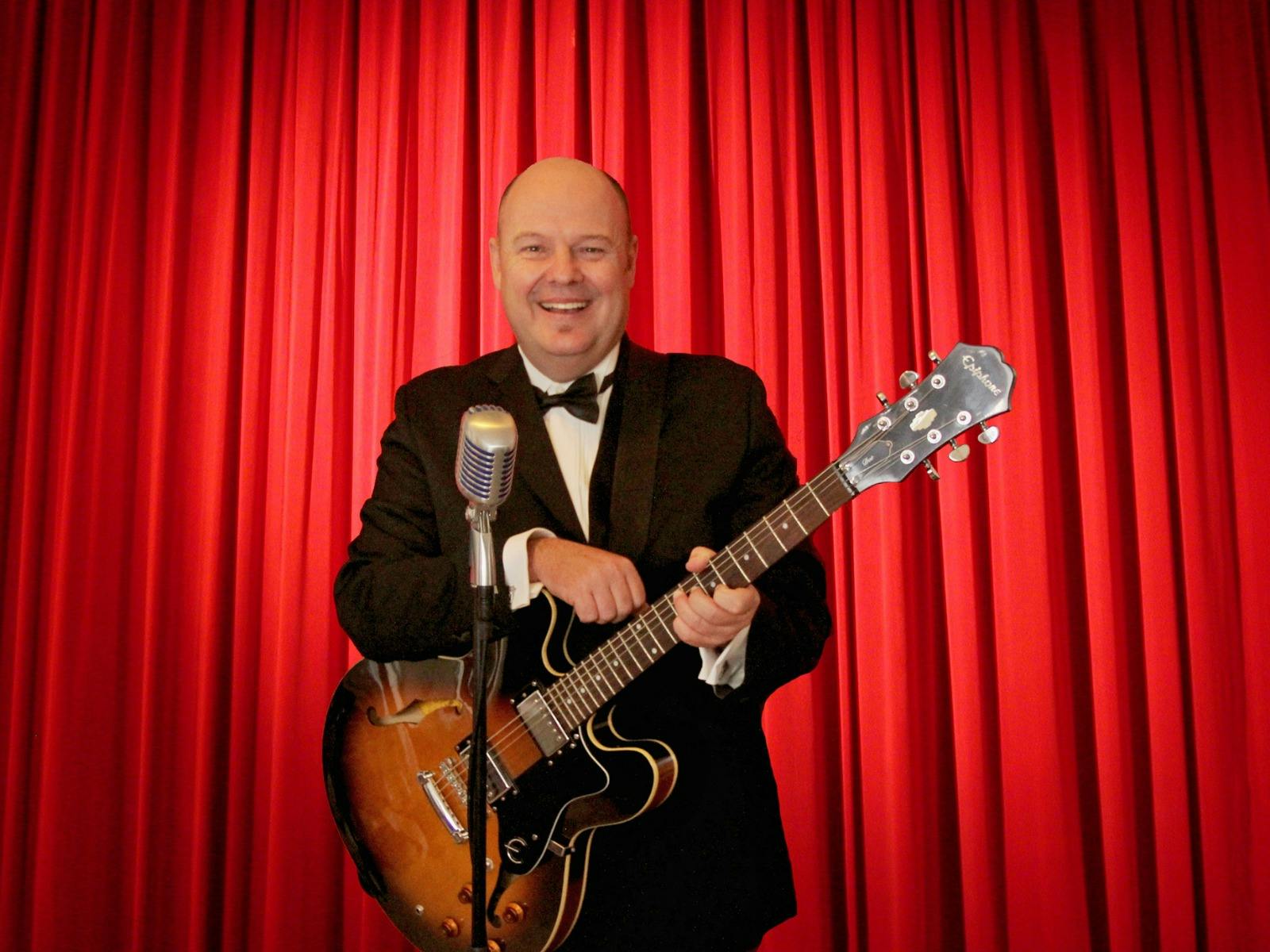 Smiling man holding a guitar - red curtains in background