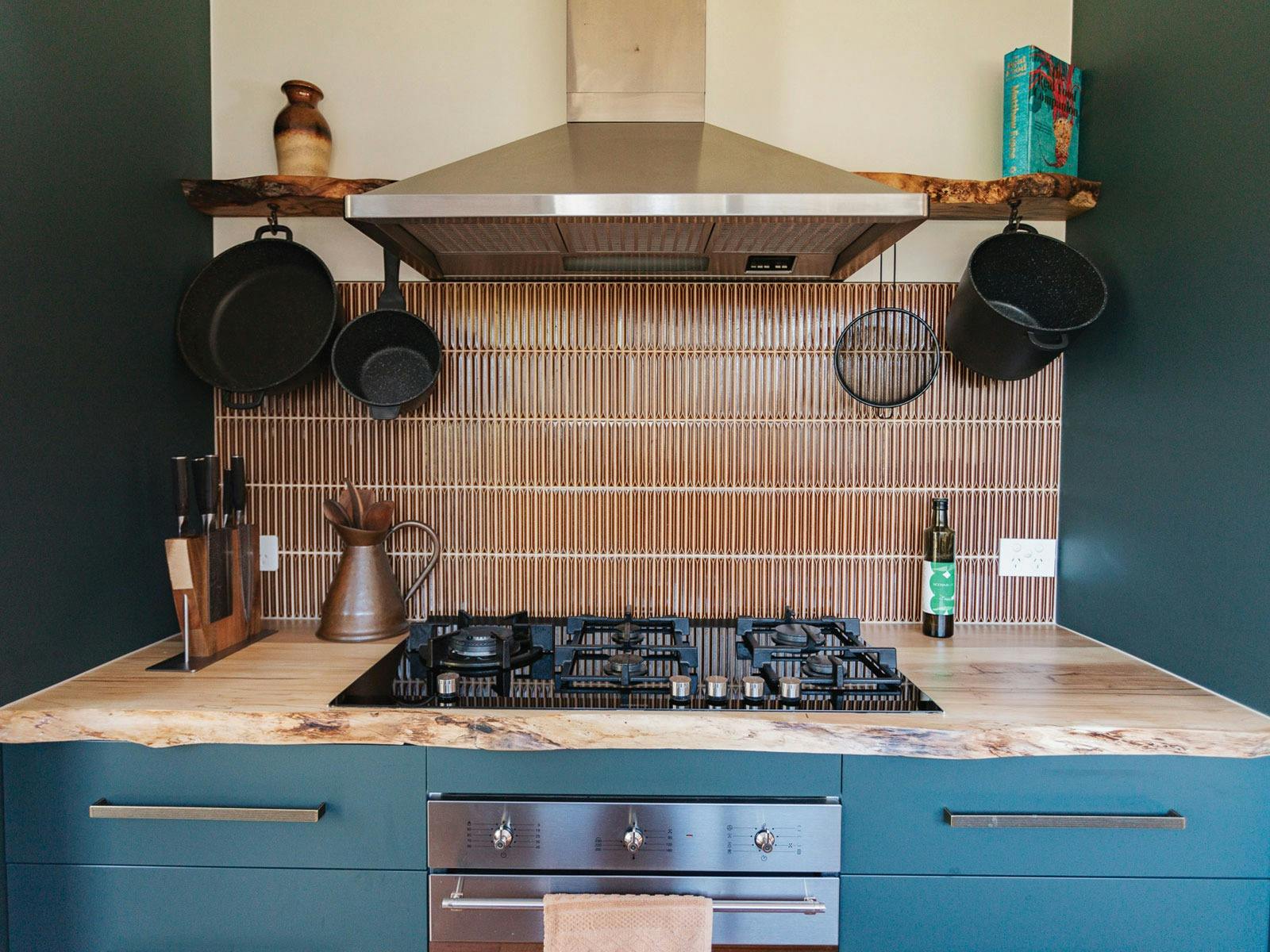 Stove, oven and rangehood with pots and pans hanging from a shelf.
