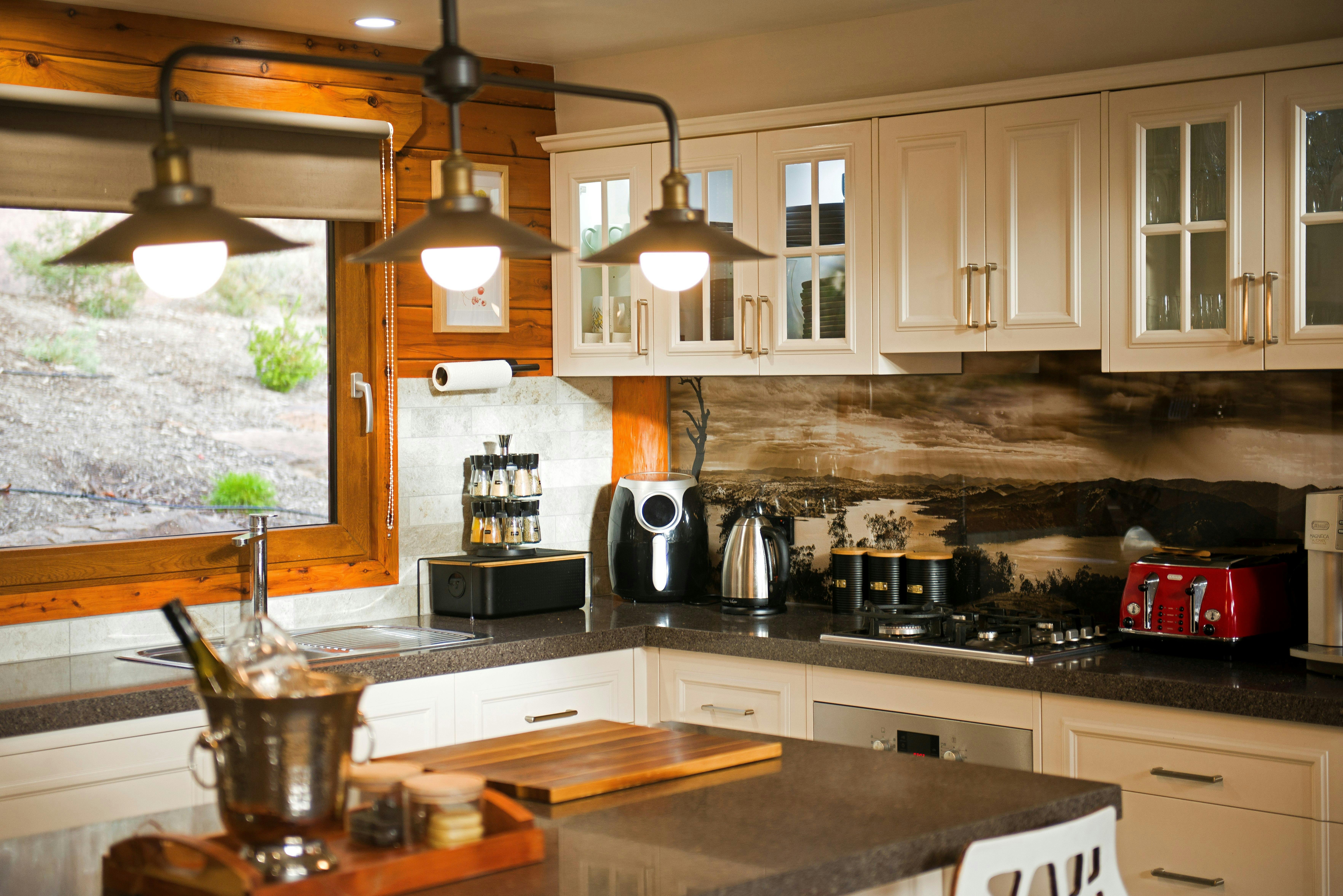 Modern kitchen with white cabinetry, pendant lighting, bushland views.