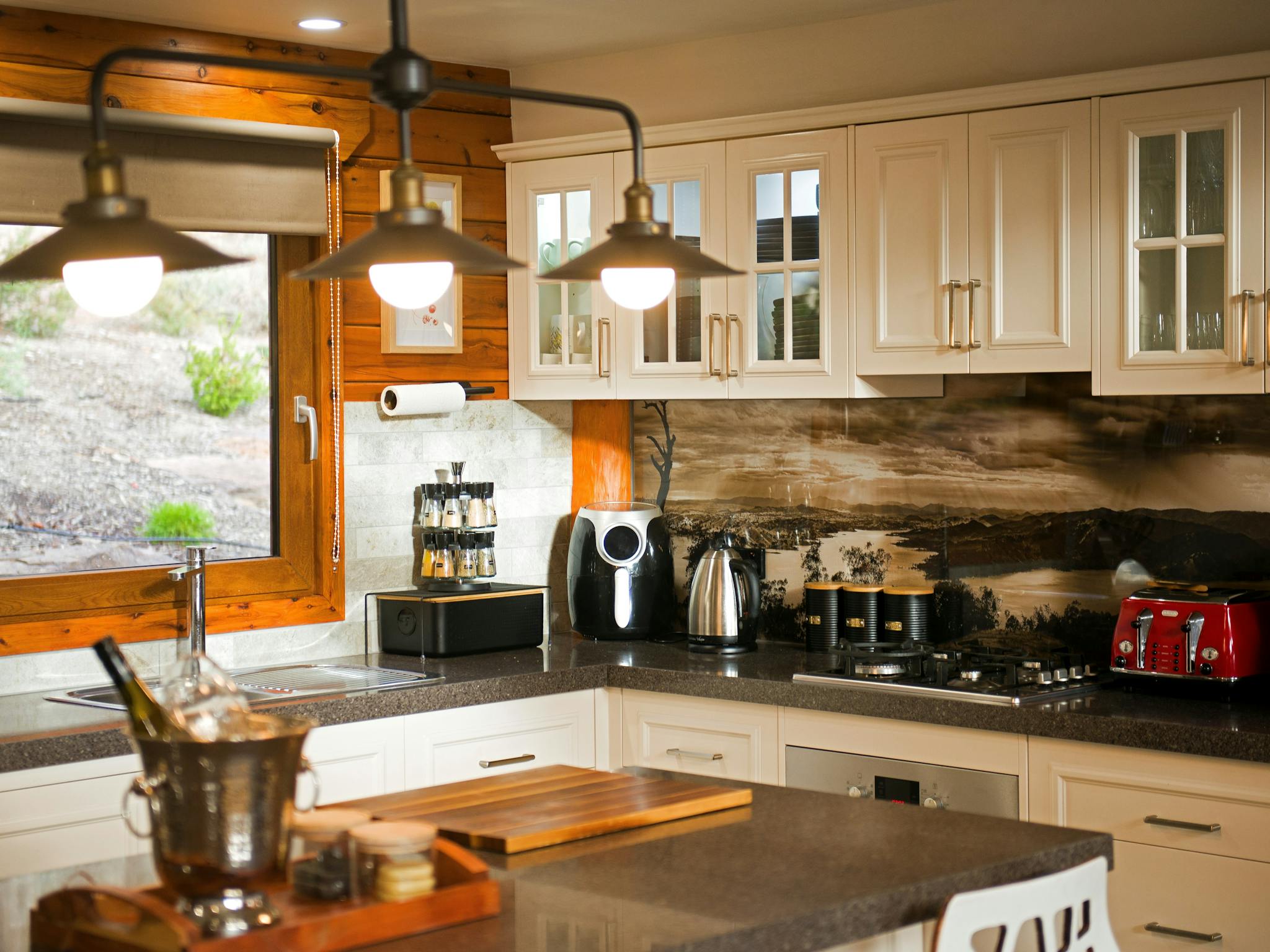 Modern kitchen with white cabinetry, pendant lighting, bushland views.
