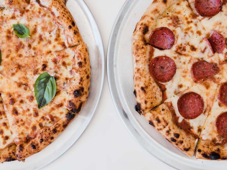Margherita pizza on the left, Pepproni pizza on the right set on white table backdrop