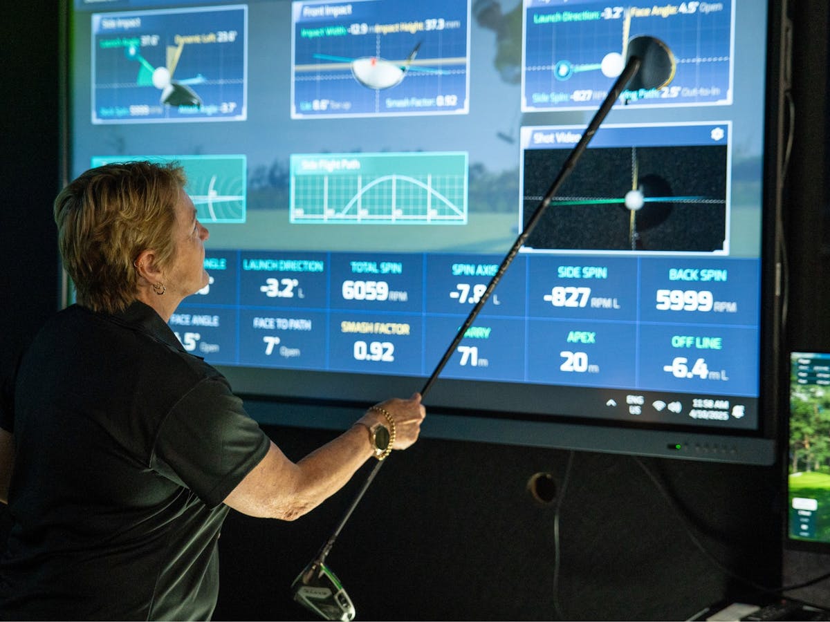 A female golf coach points at data from the golf simulator using a club to explain A female golf coach points at data from the golf simulator using a club to explain