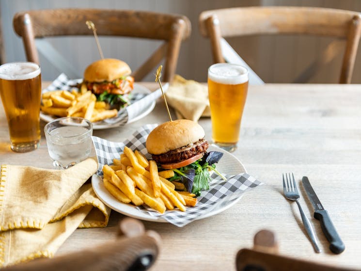 Two beef burgers and two schooners of beer on a wooden table