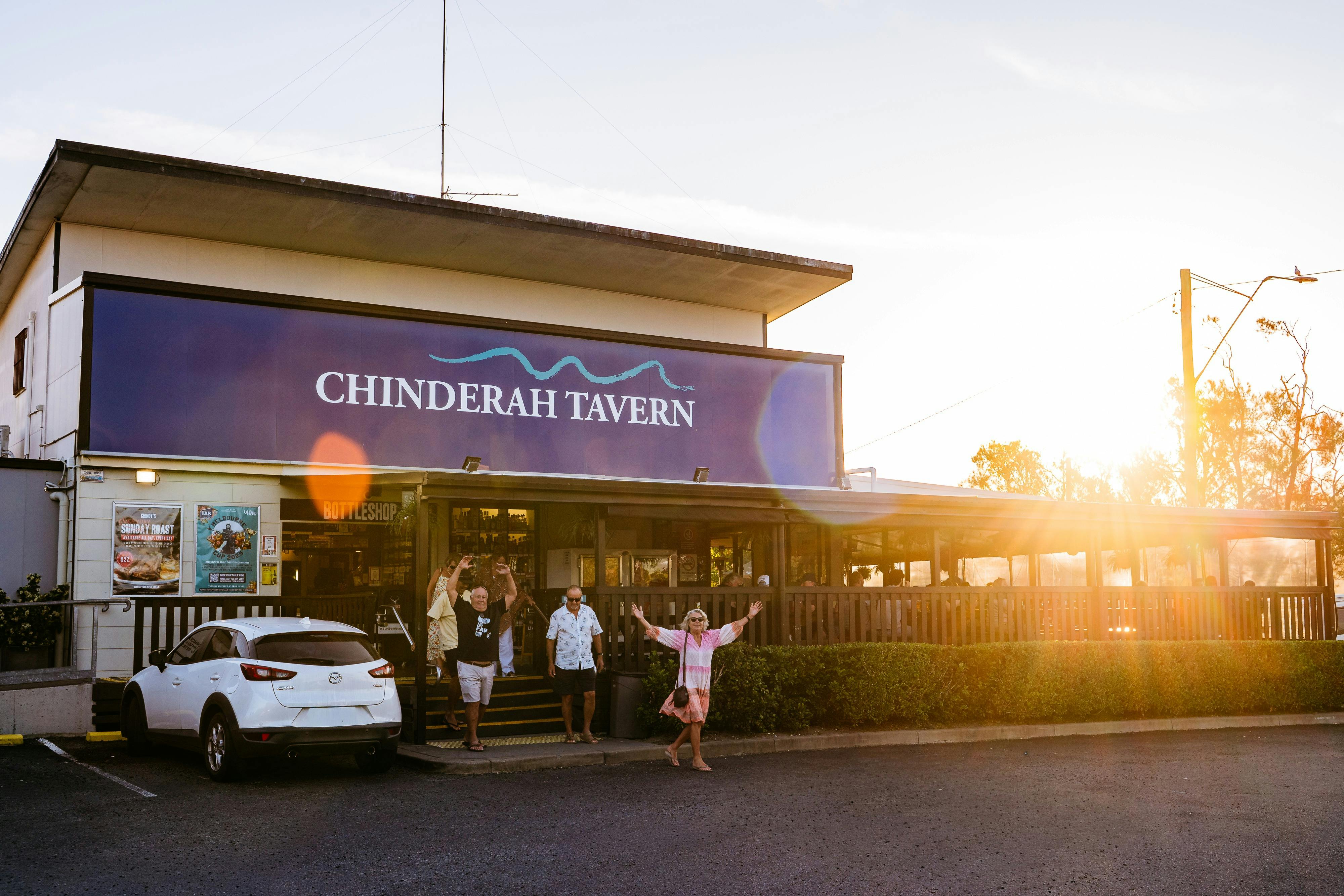 A group of people walking out of the Chinderah Tavern entrance at sunset