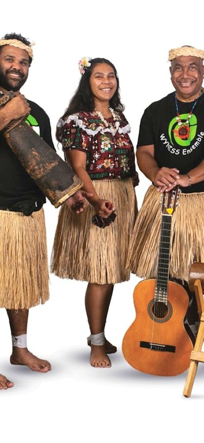 4 musicians stand, wearing grass skirts, holding a guitar and wooden percussion instruments