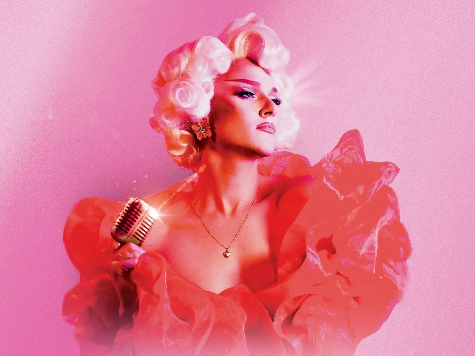 Glamorous drag queen with mic is front of pink backdrop