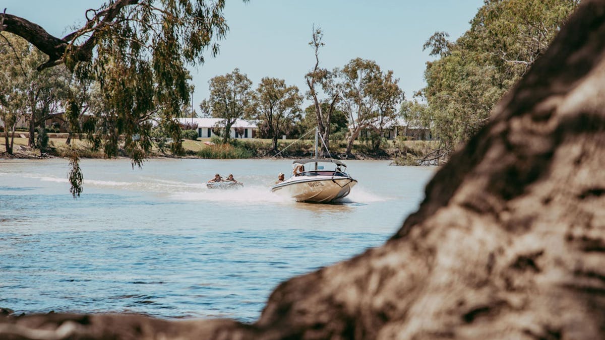 A boat is pulling along kids on a tube in the water at the Goondiwindi Water Park