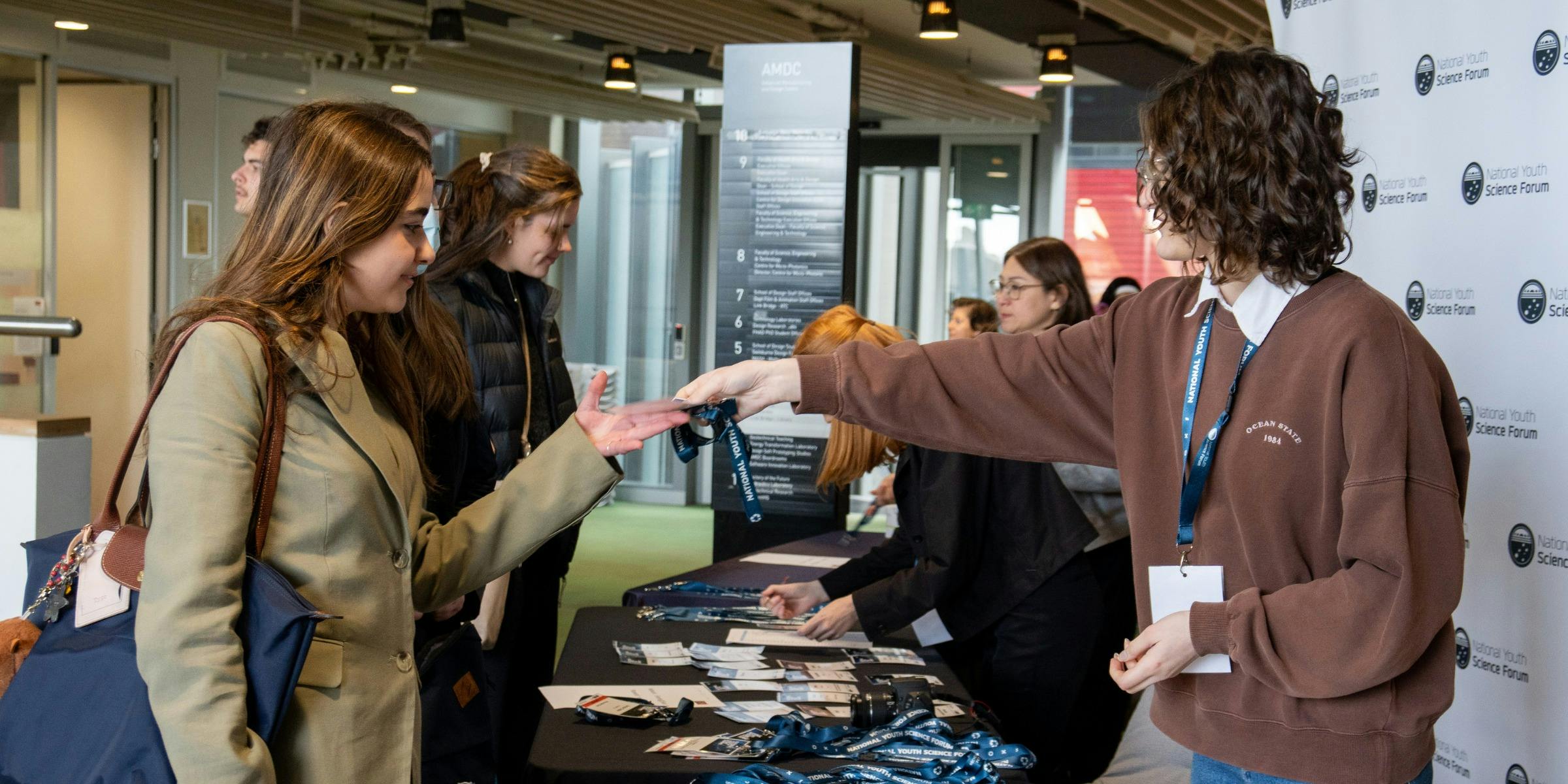 Two attendees collecting their conference lanyards from staff at a registration table