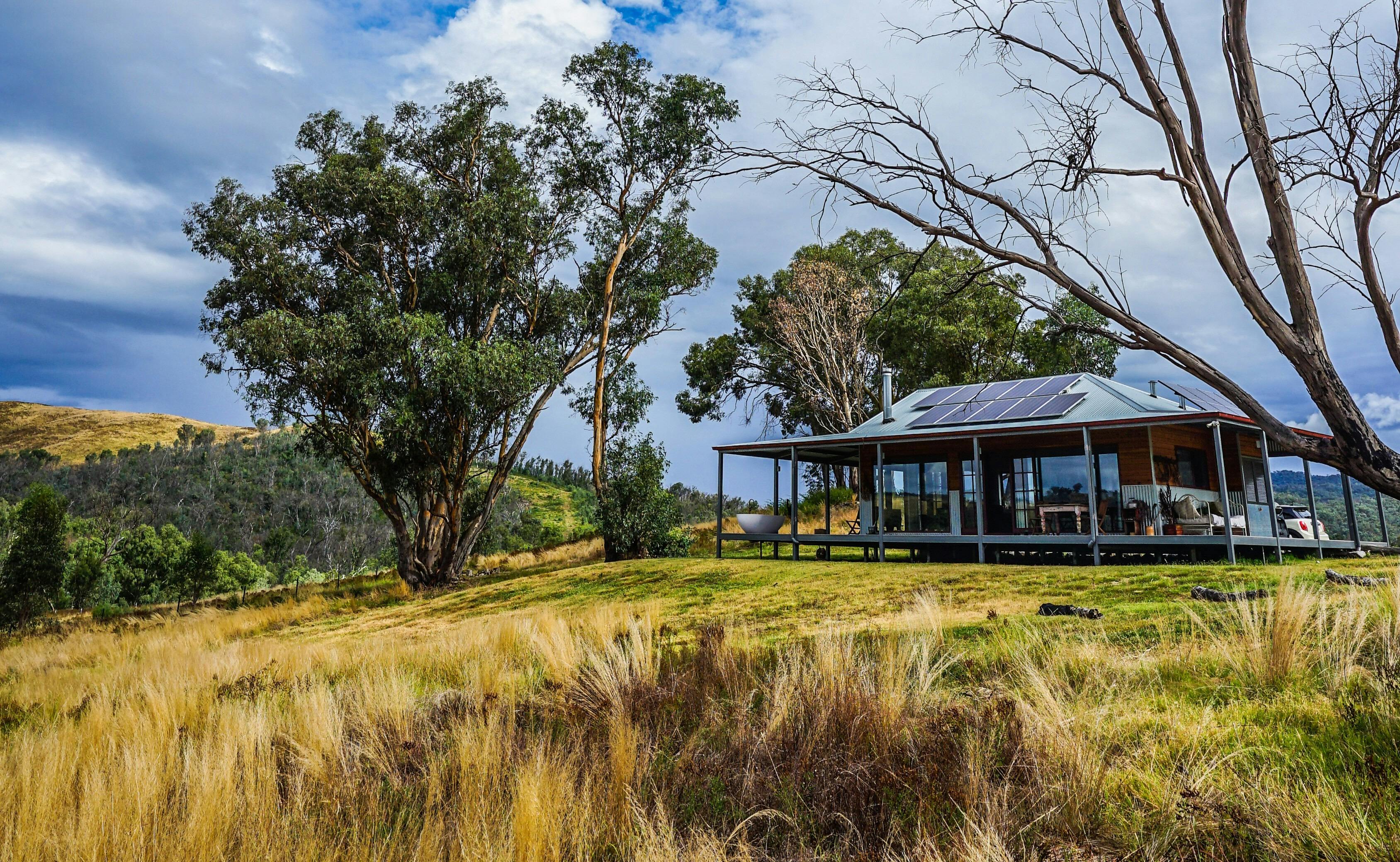 広いベランダのあるモダンで素朴な小屋が、青い空を背景に金色の芝生の上に建っています。