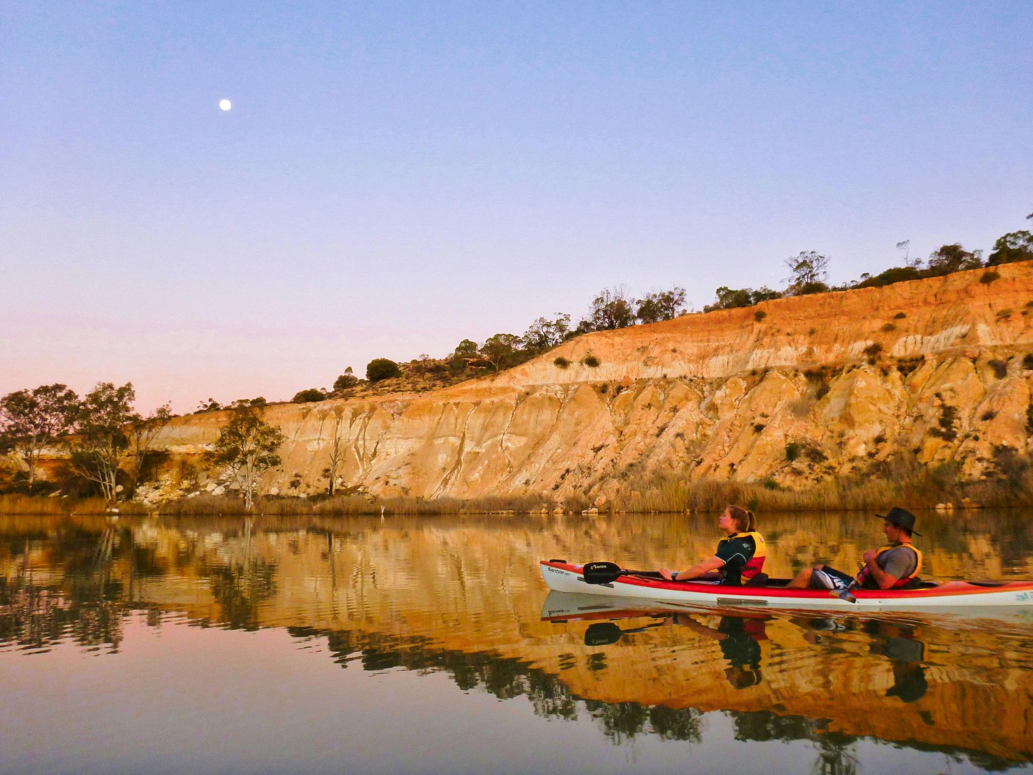Kayak floating in the reflection of cliffs on the water, with the afterglow of senset in the sky.