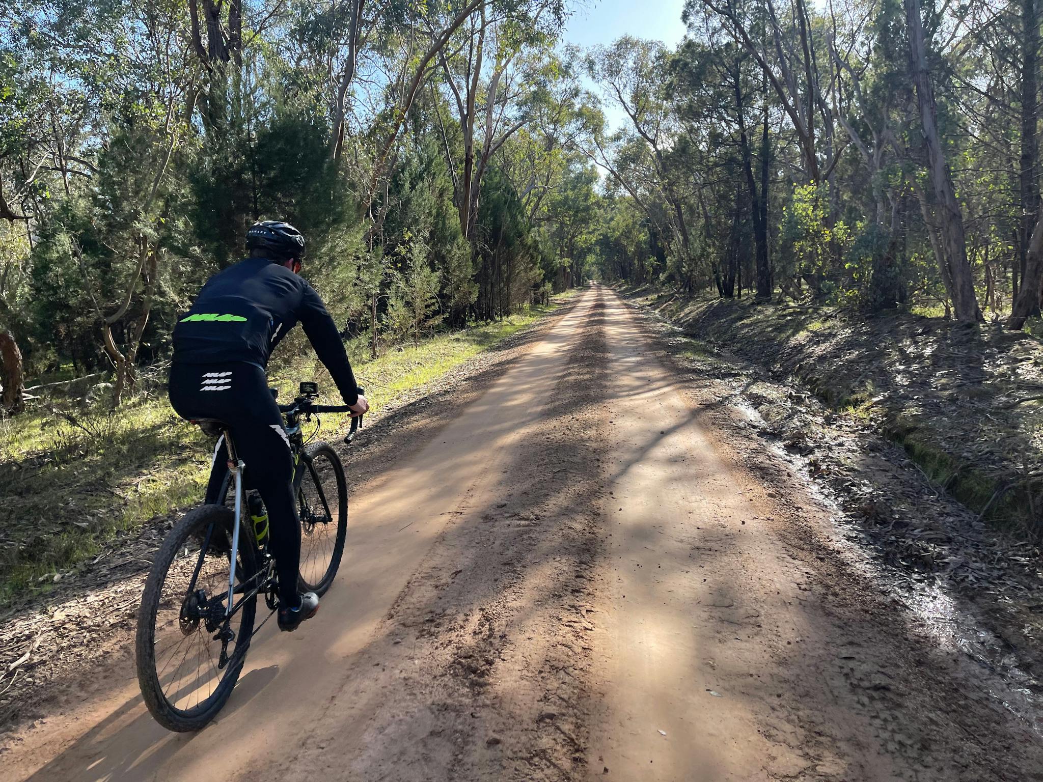 Cyclist on a gravel road with bushy trees on both sides of road