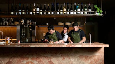 Three chefs—one particularly good looking—preparing a meal behind a bench made of Italian marble