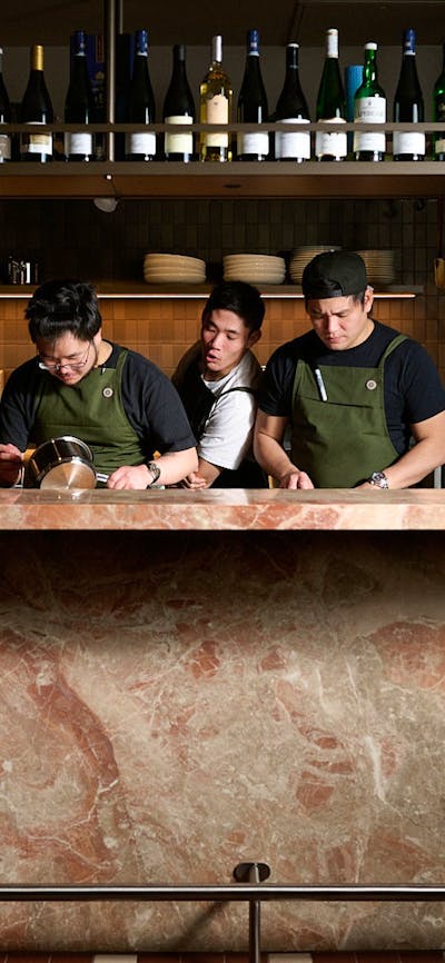 Three chefs—one particularly good looking—preparing a meal behind a bench made of Italian marble