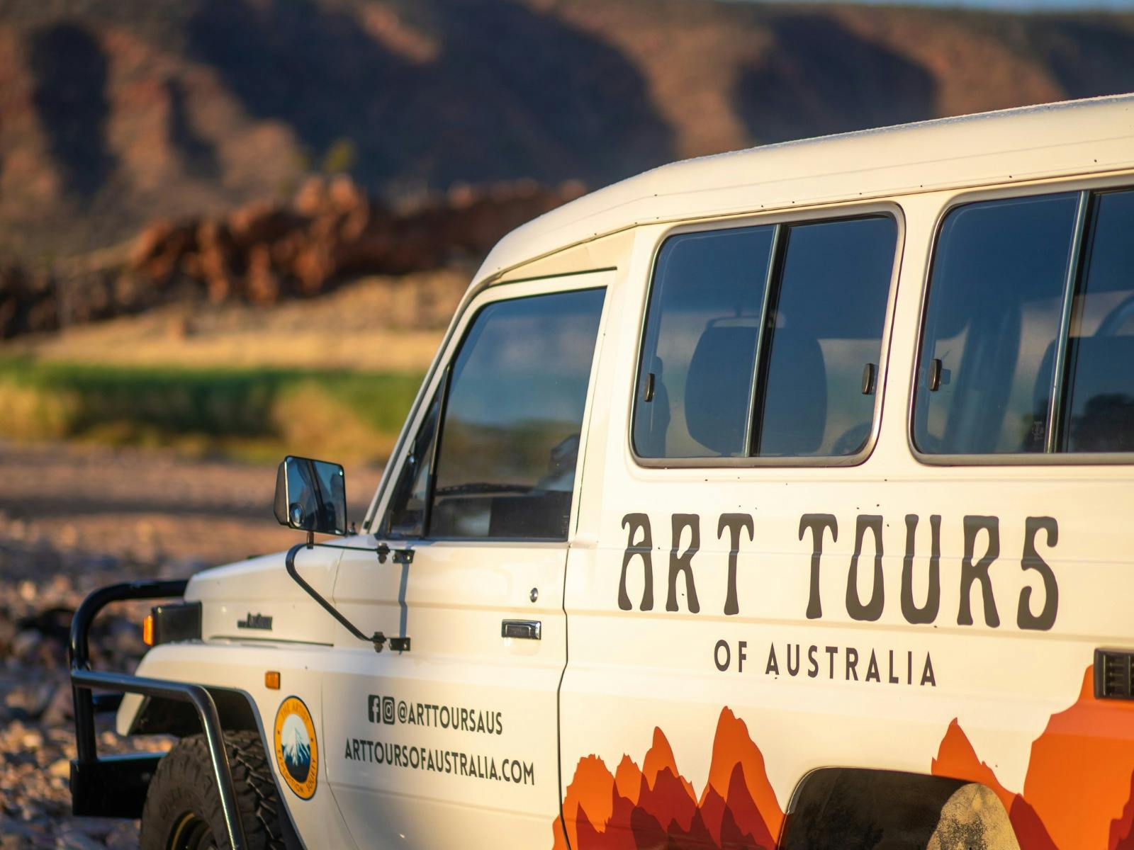 An off-road vehicle with "Art Tours of Australia" branding is parked in a desert-like landscape.