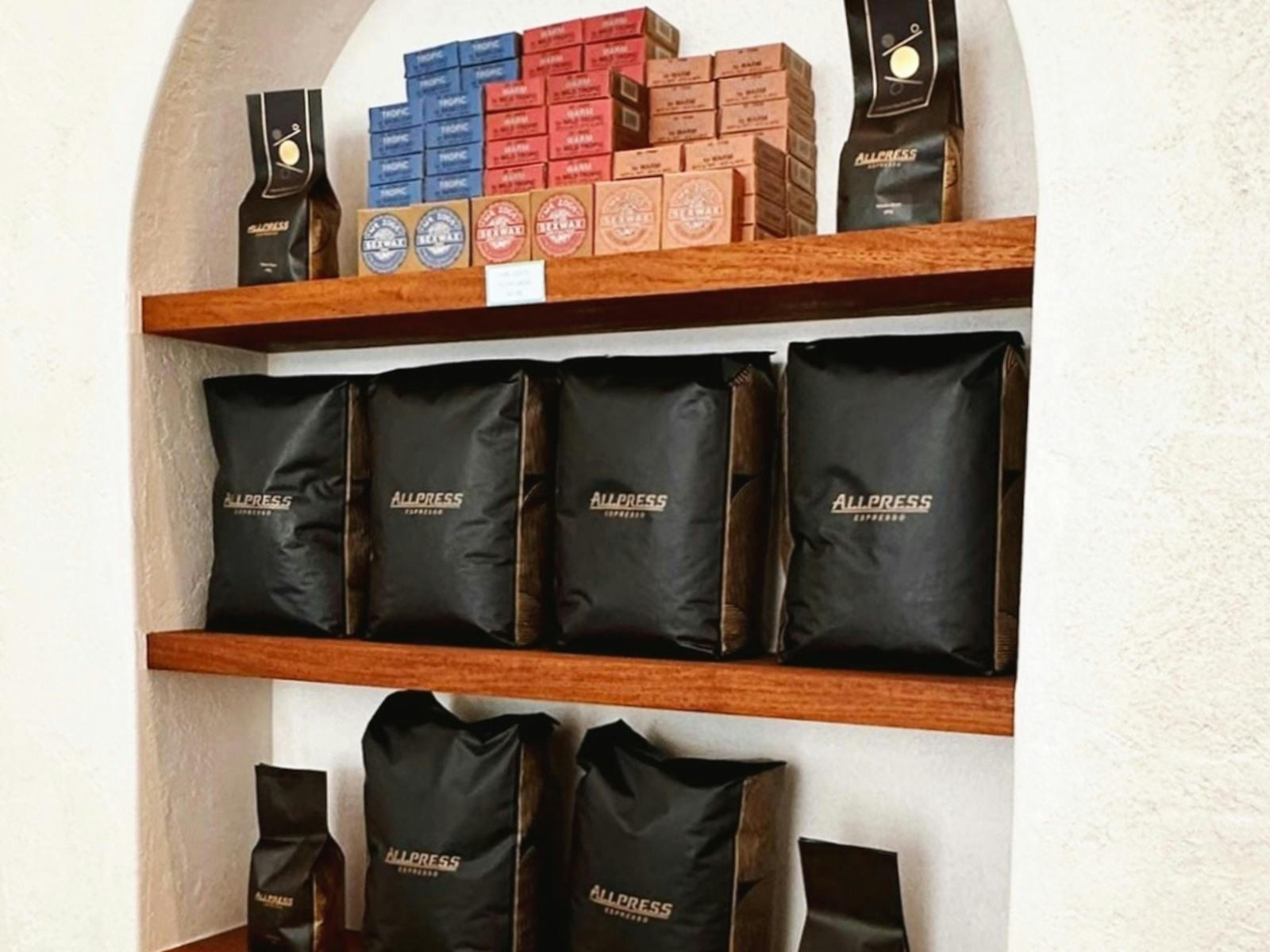 Coffee beans and surf wax on timber shelves in front of a white wall