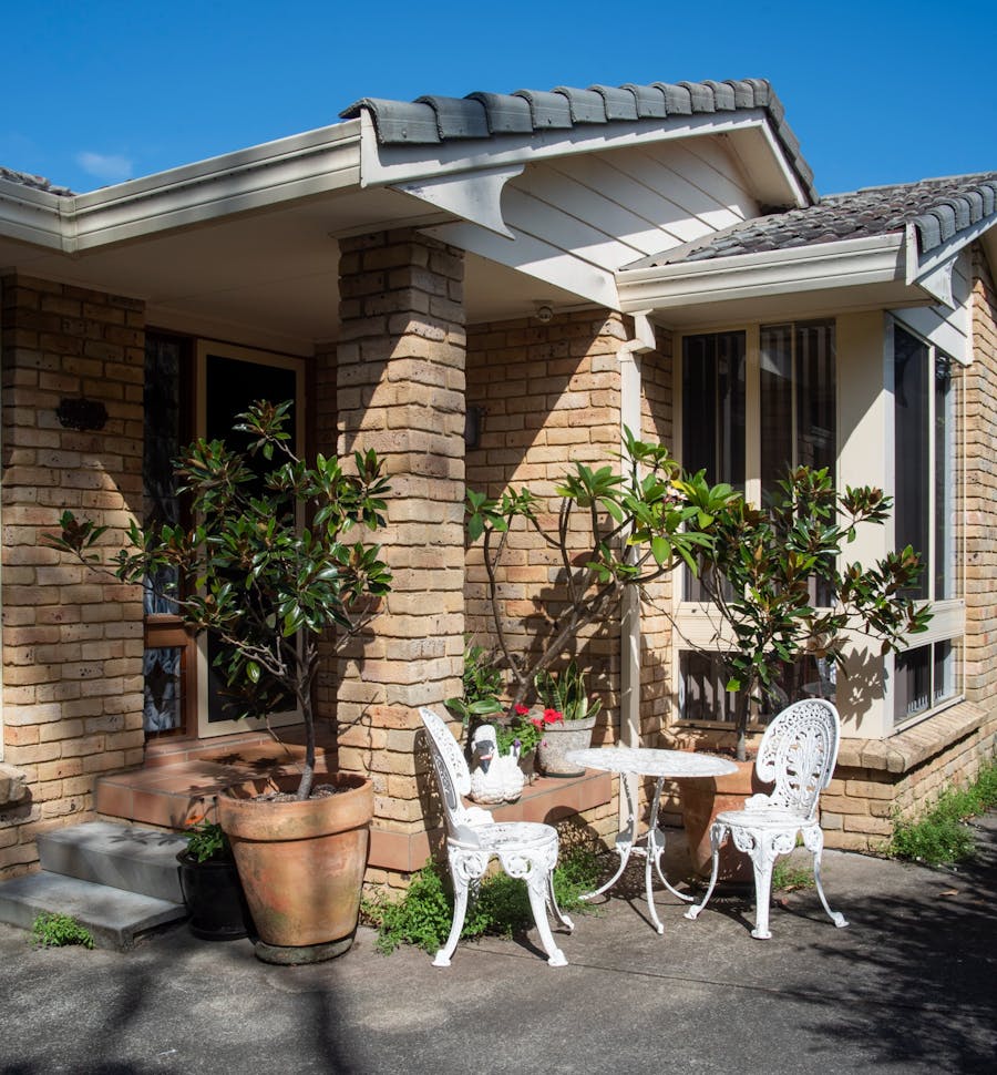 Front door with two steps up to a small patio. Wrought Iron table and chairs with garden setting