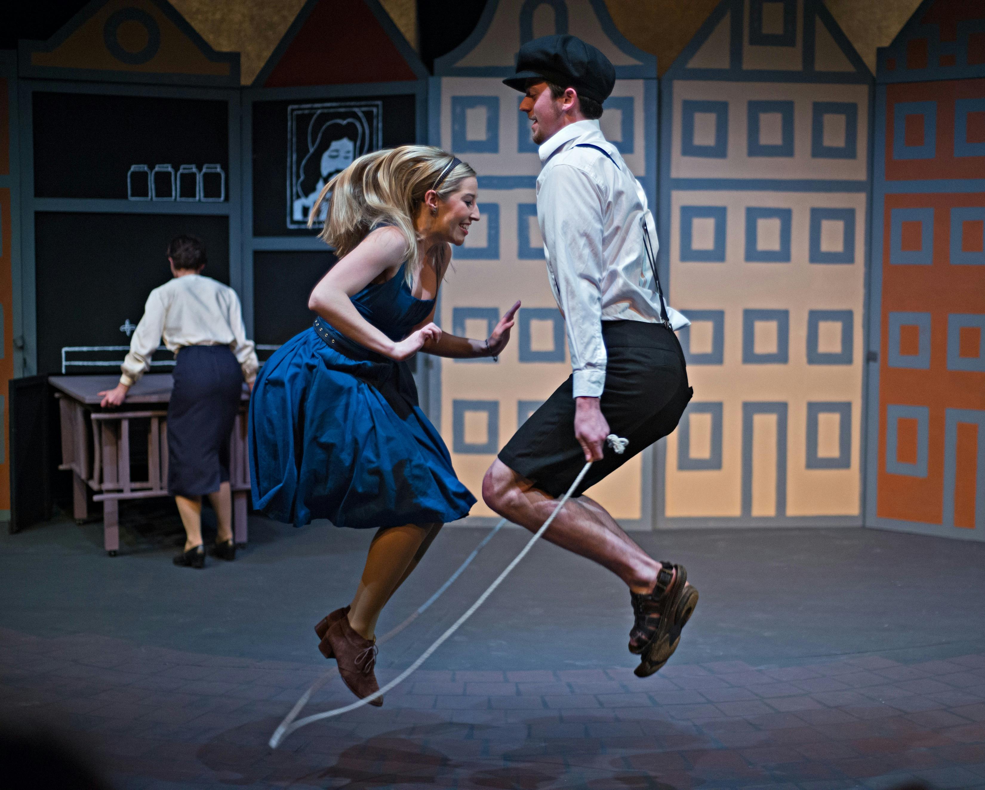 a young blond female wears a blue dress and jumps rope with a young man in white shirt and breeches