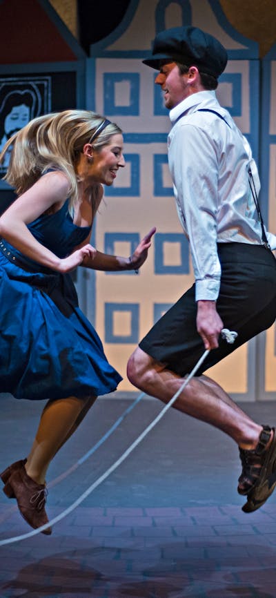 a young blond female wears a blue dress and jumps rope with a young man in white shirt and breeches