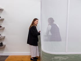 Image of femme person speaking to a staff member. The staff member is obscured by a panel of white m