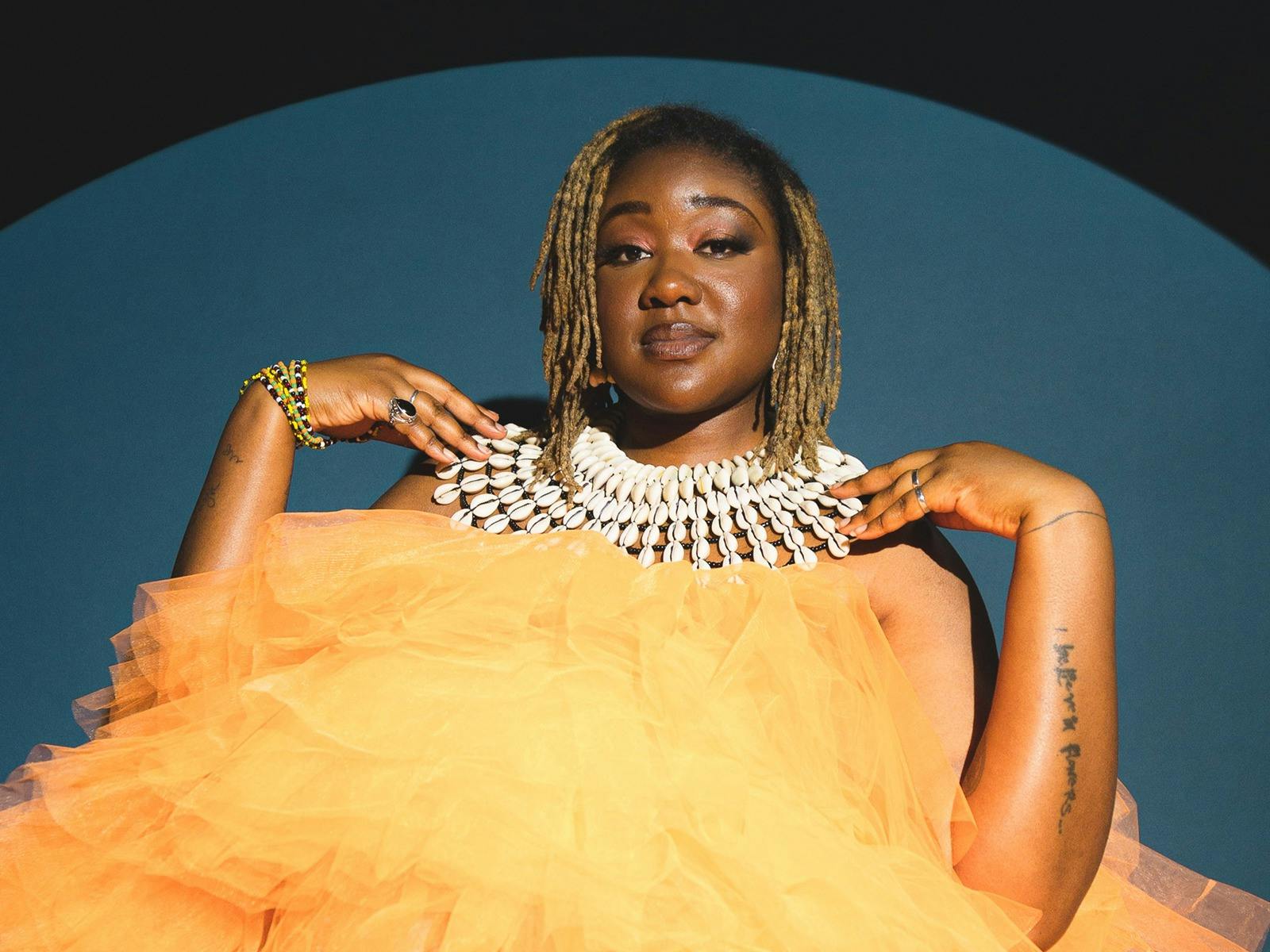 A mid shot portrait of Haitian performer and musician Nancy Denis. She wears a dress of yellow tule