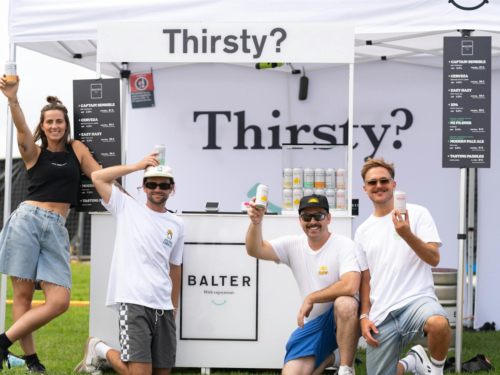 4 people stand outside a beer stall holding beers