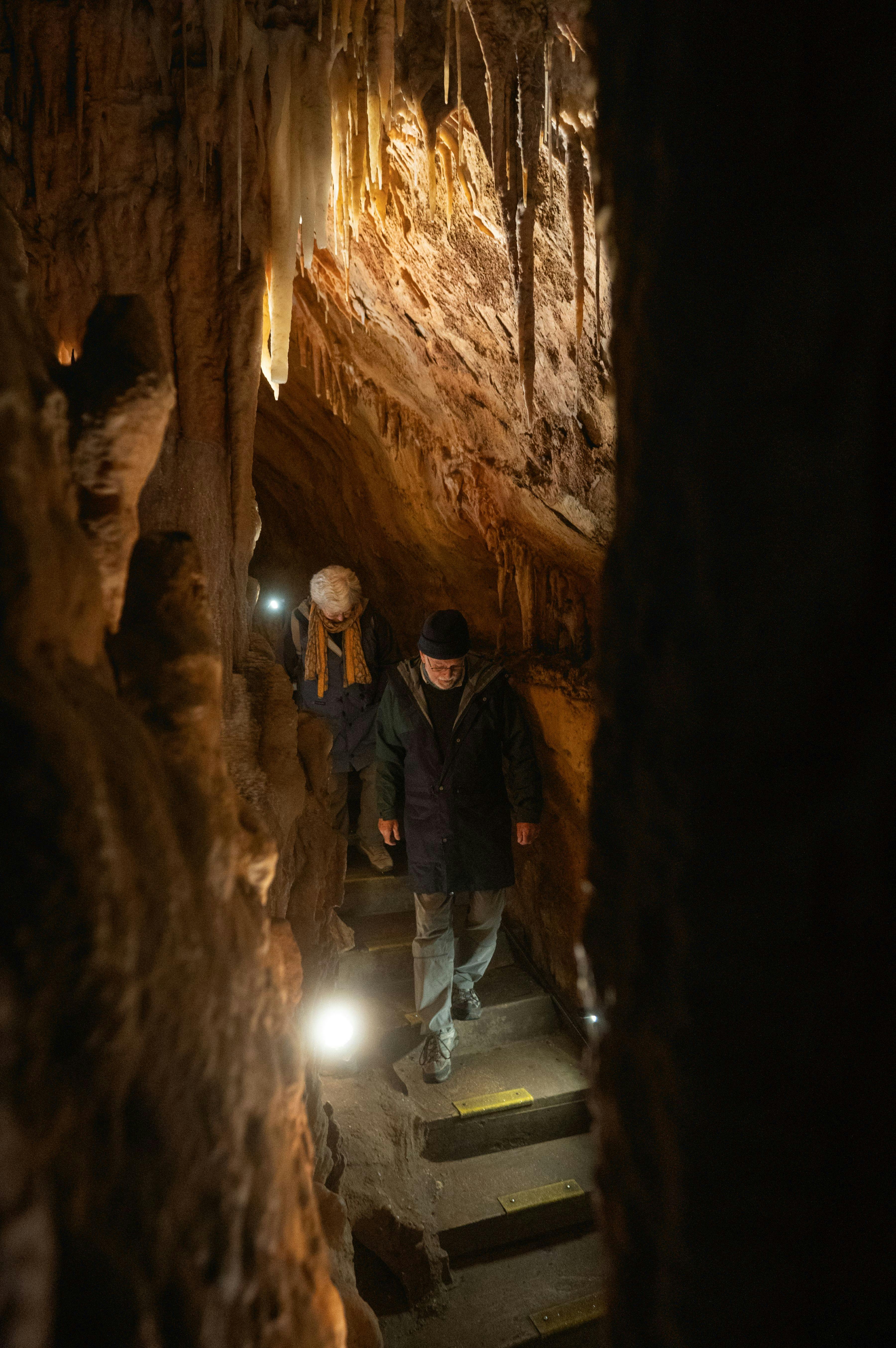 A man and a woman behind descending a staircase within the Cave as part of the tour; a narrow path