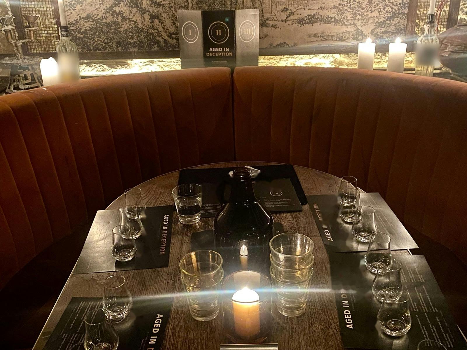 A candlelit table set for five with tasting glasses and mats, in a curved velvet booth