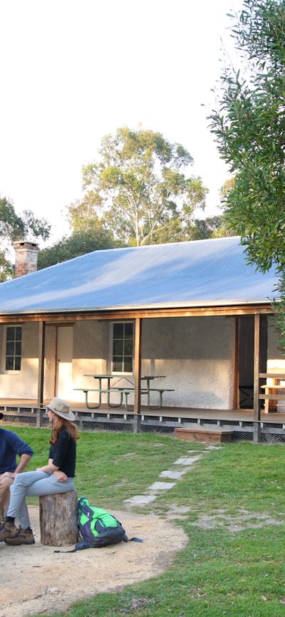 3 people sitting around a firepit among green grass and Heritage property in background