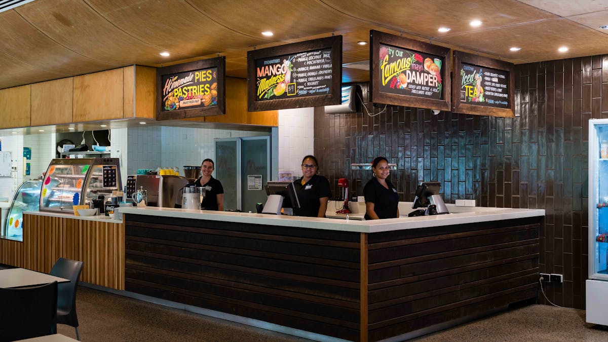 Two staff member stand behind the counter smiling, with menu signs displaying above