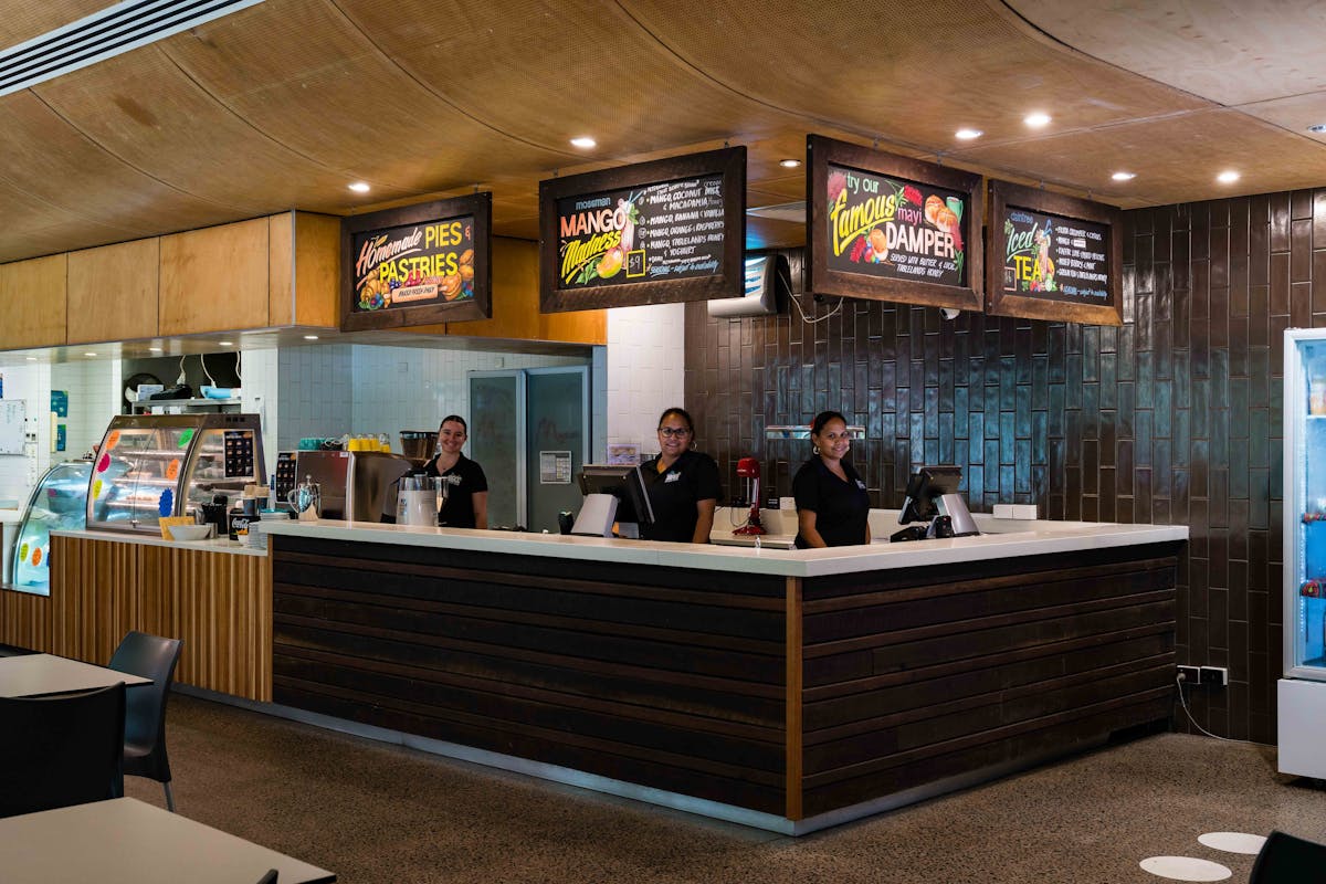 Two staff member stand behind the counter smiling, with menu signs displaying above