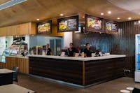 Two staff member stand behind the counter smiling, with menu signs displaying above