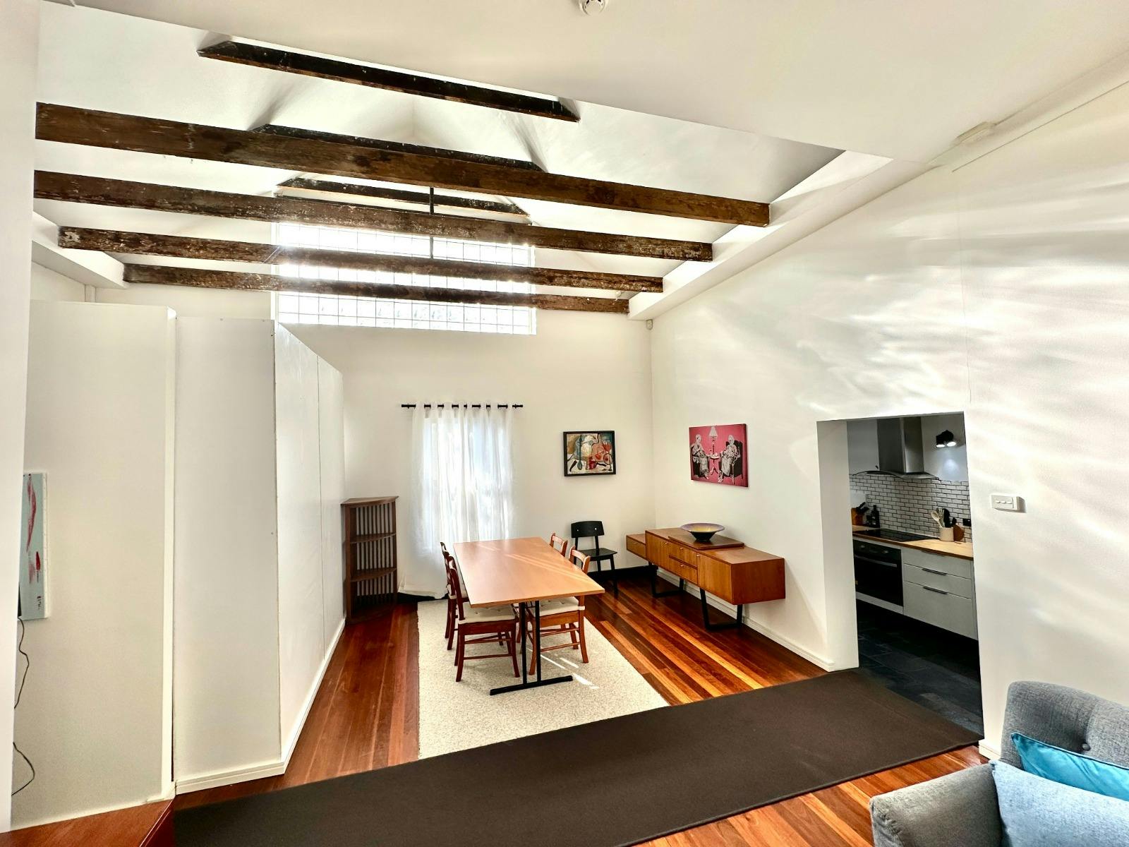 Open-plan living and dining area with timber floors and feature ceiling beams.