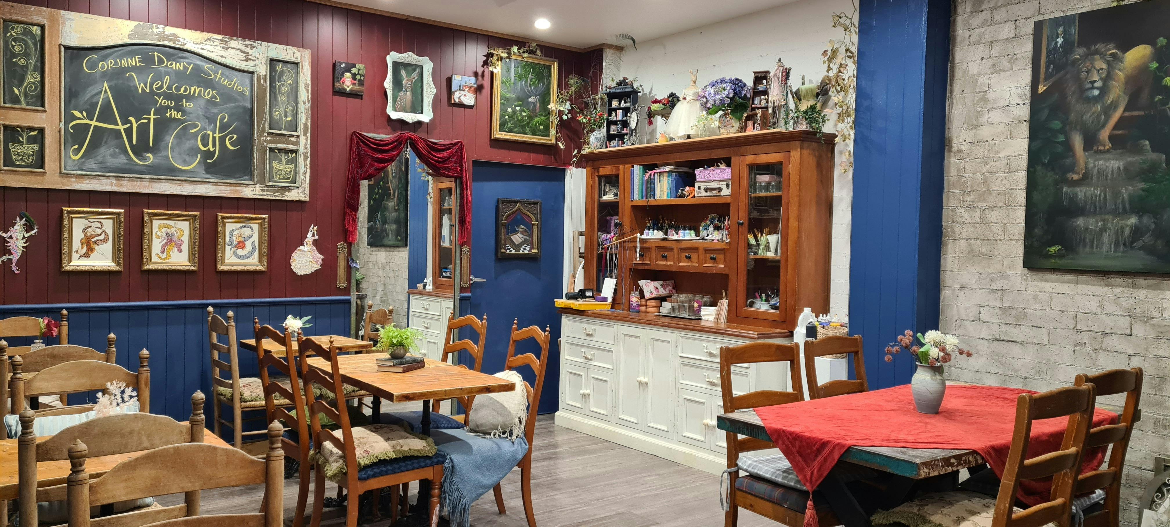 Blue and red walls, cafe style table and chairs in an art room with artworks all over the walls.