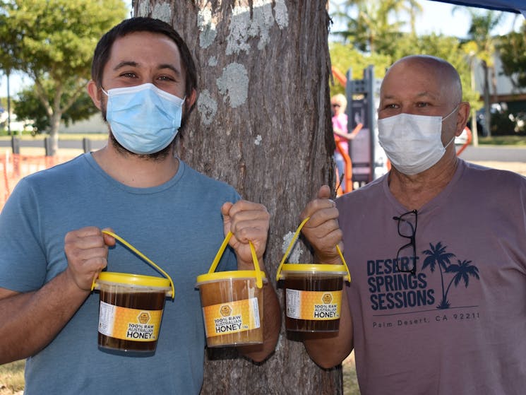 Two men holding buckets of honey.