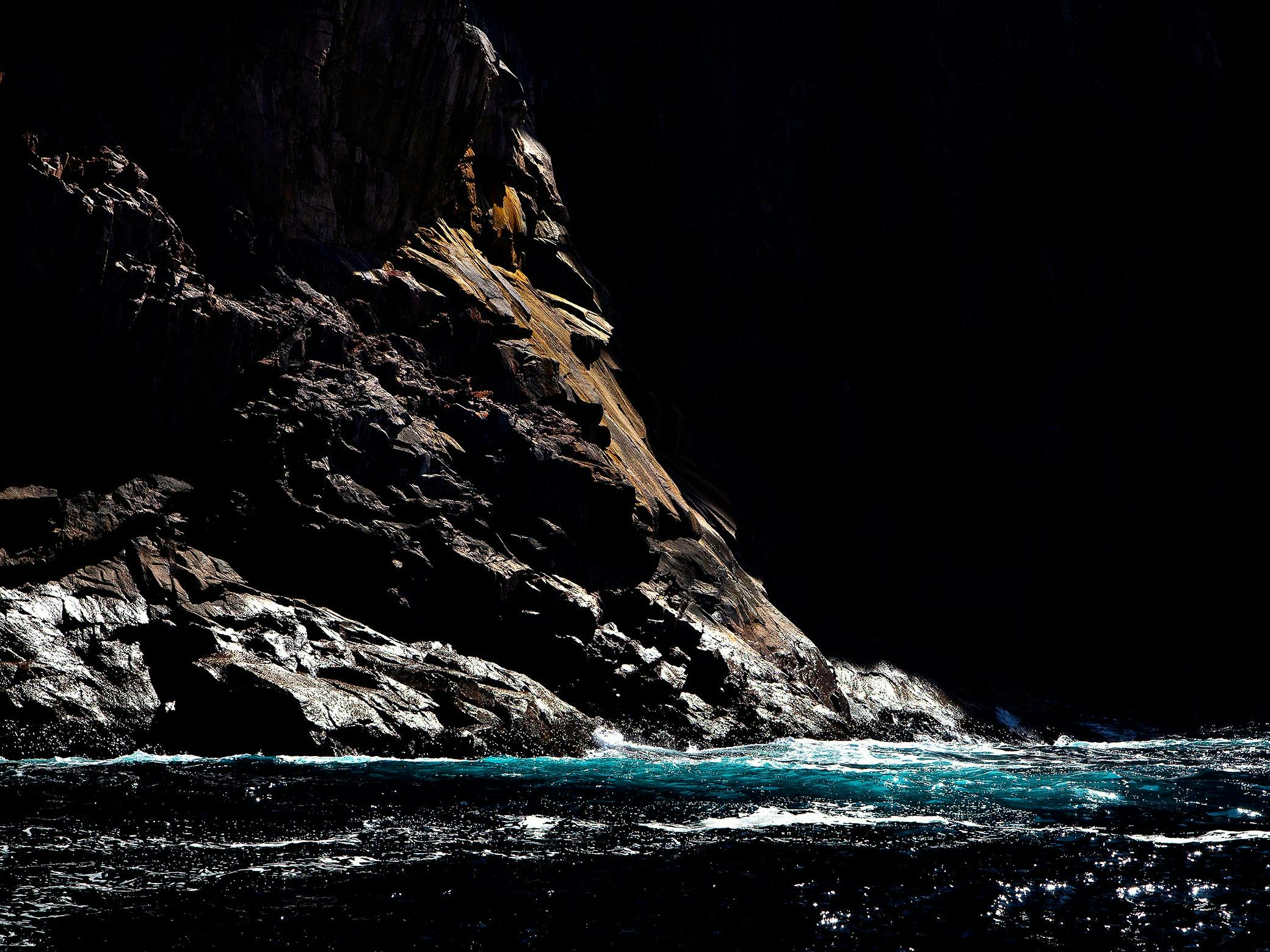 A shaft of light falls dramatically on a cliff face and lights up the turquoise water