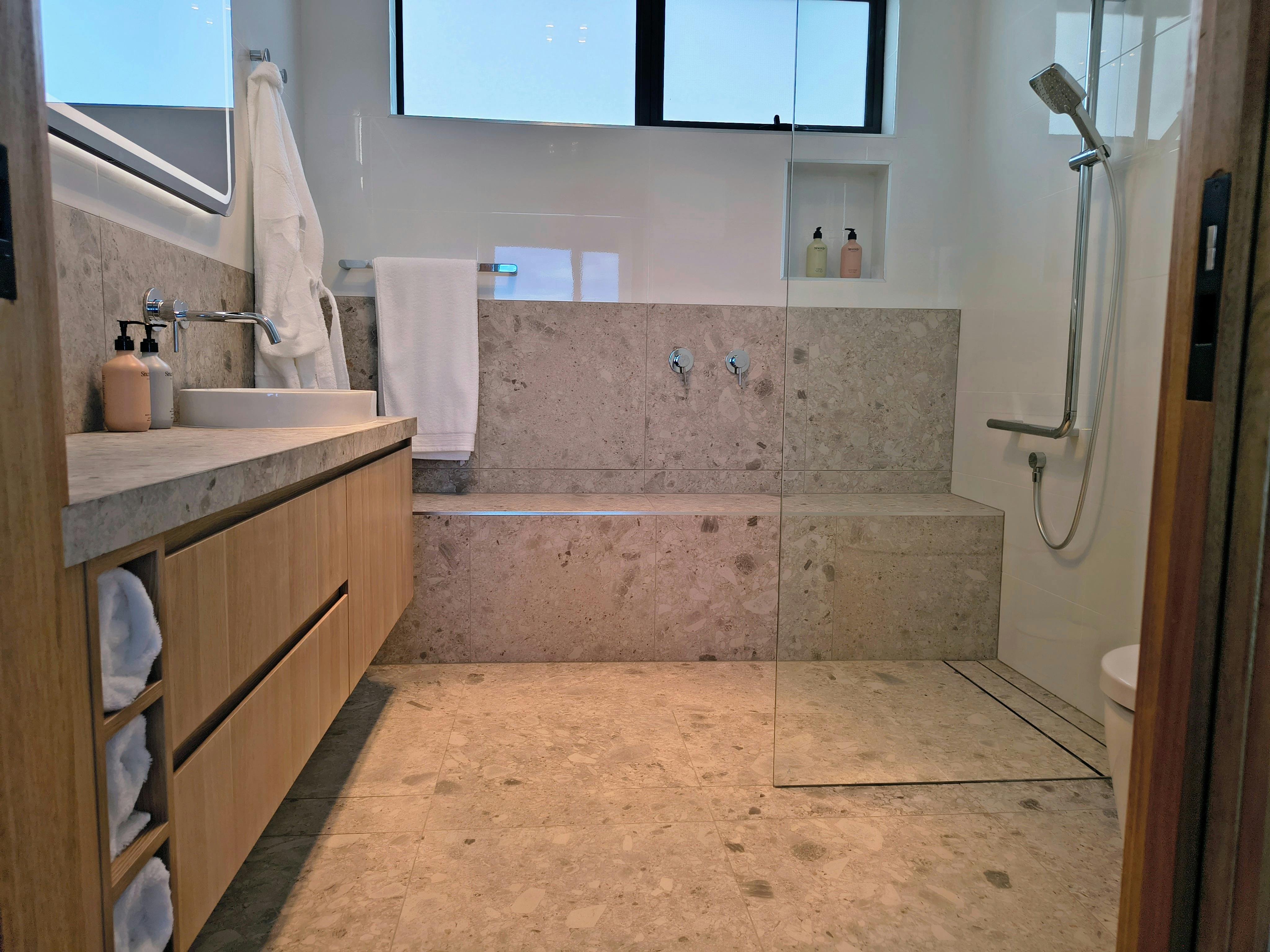 Bathroom at Sand Shacks has over height toilet, hand rails and bench seat styled for day spa vibes