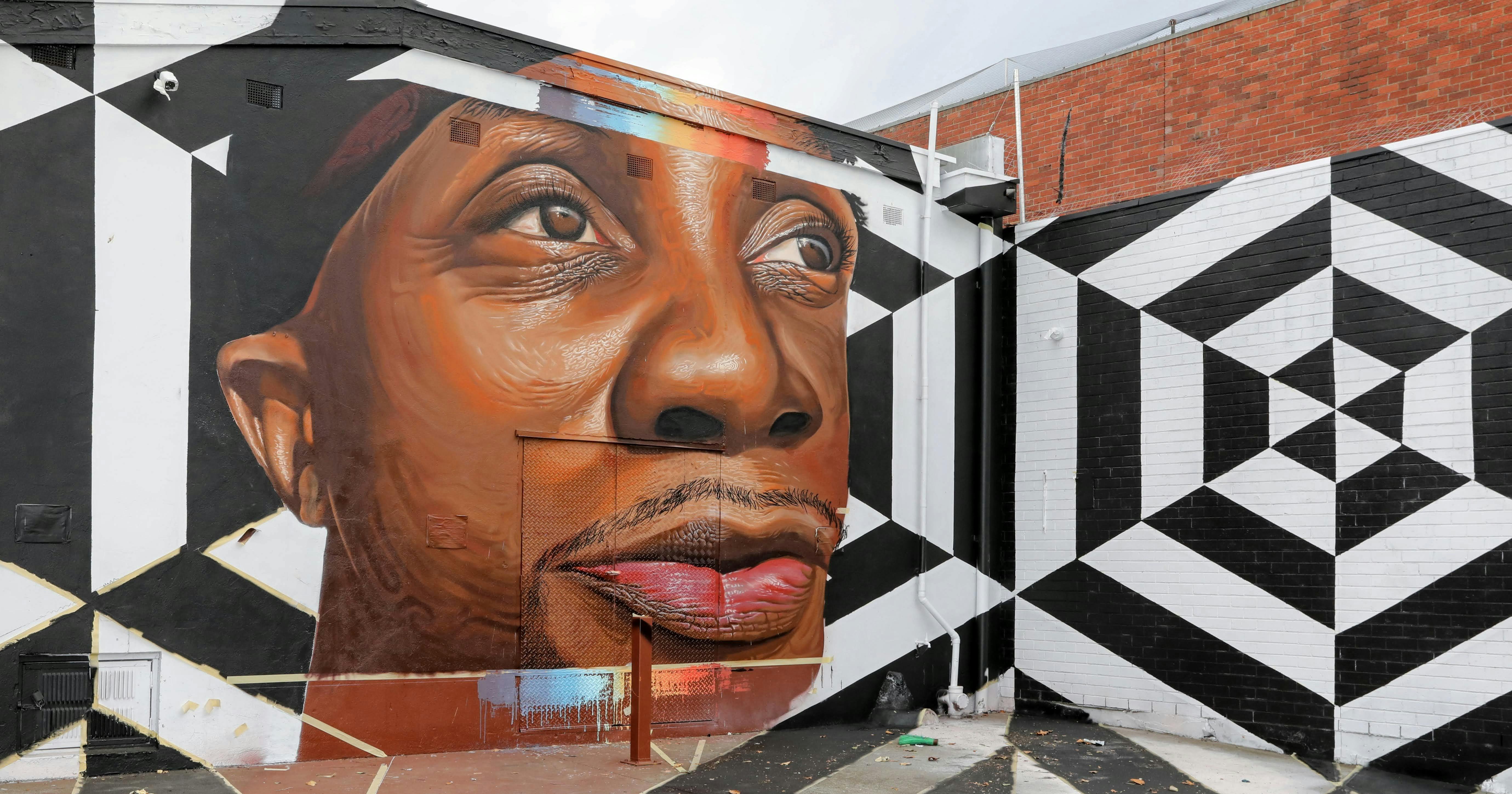 An Indigenous man looks into the distance, with black & white stripes behind with a touch of colour