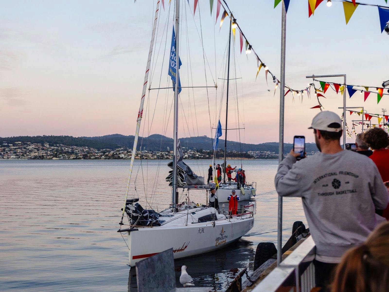 A person films a yacht arriving at the pier after the Sydney to Hobart Yacht Race.