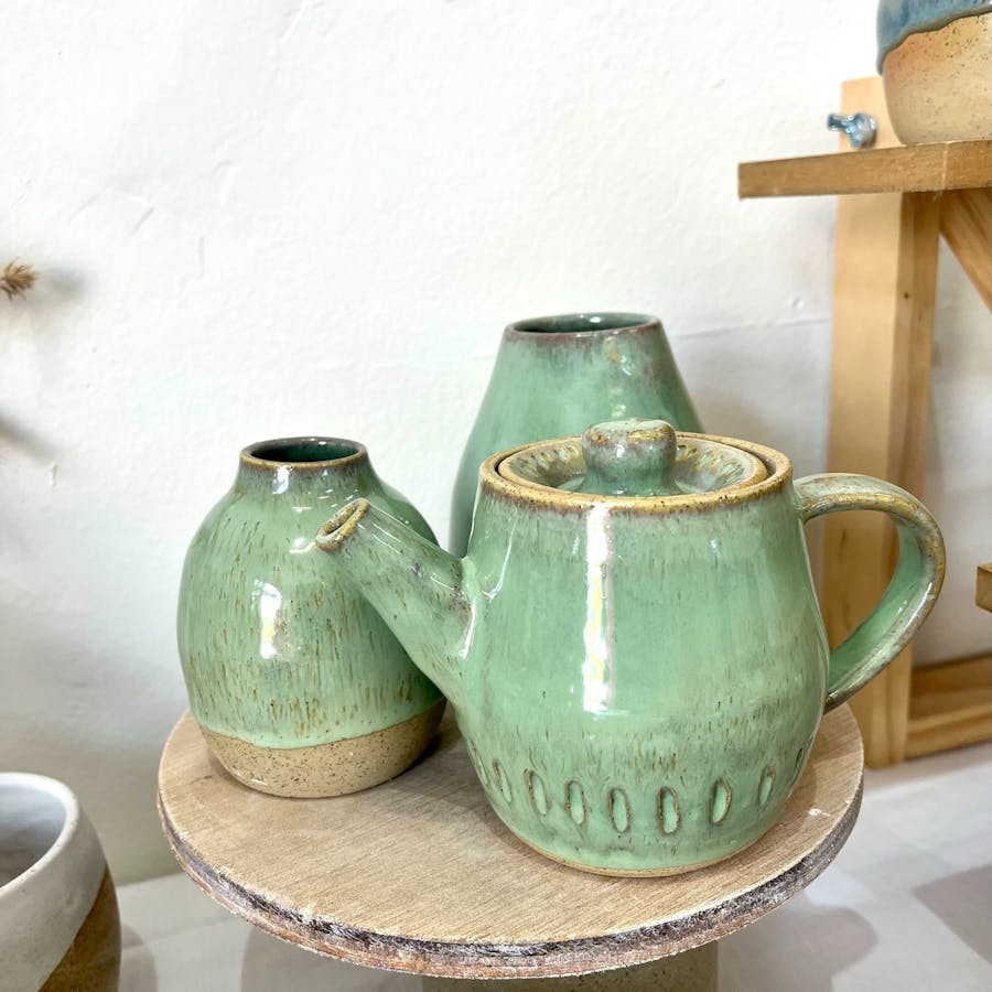 Image shows a handmade teapot in green glaze with two vases