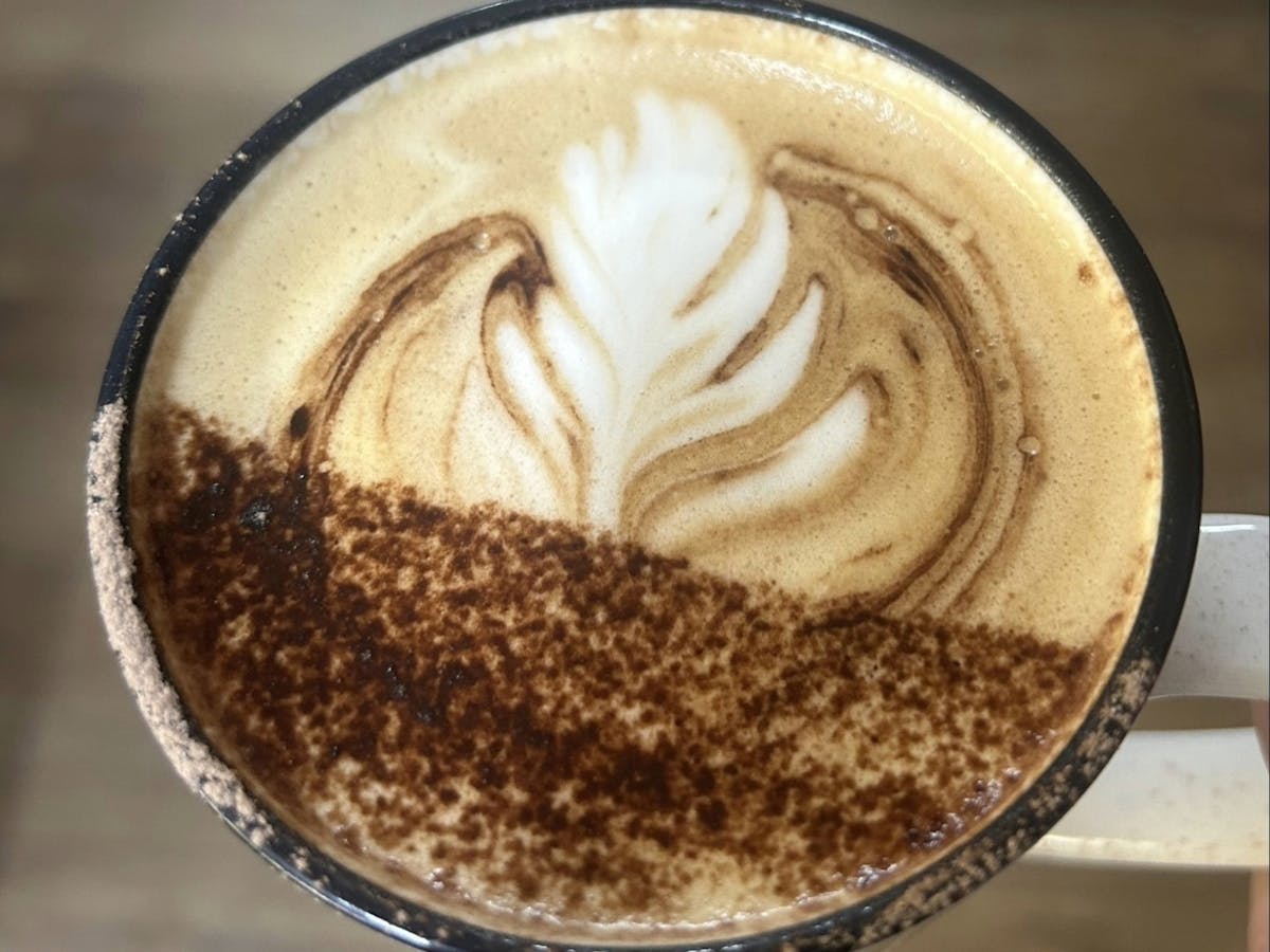 A close-up of a coffee cup with latte art in the shape of a leaf, dusted with cocoa powder.