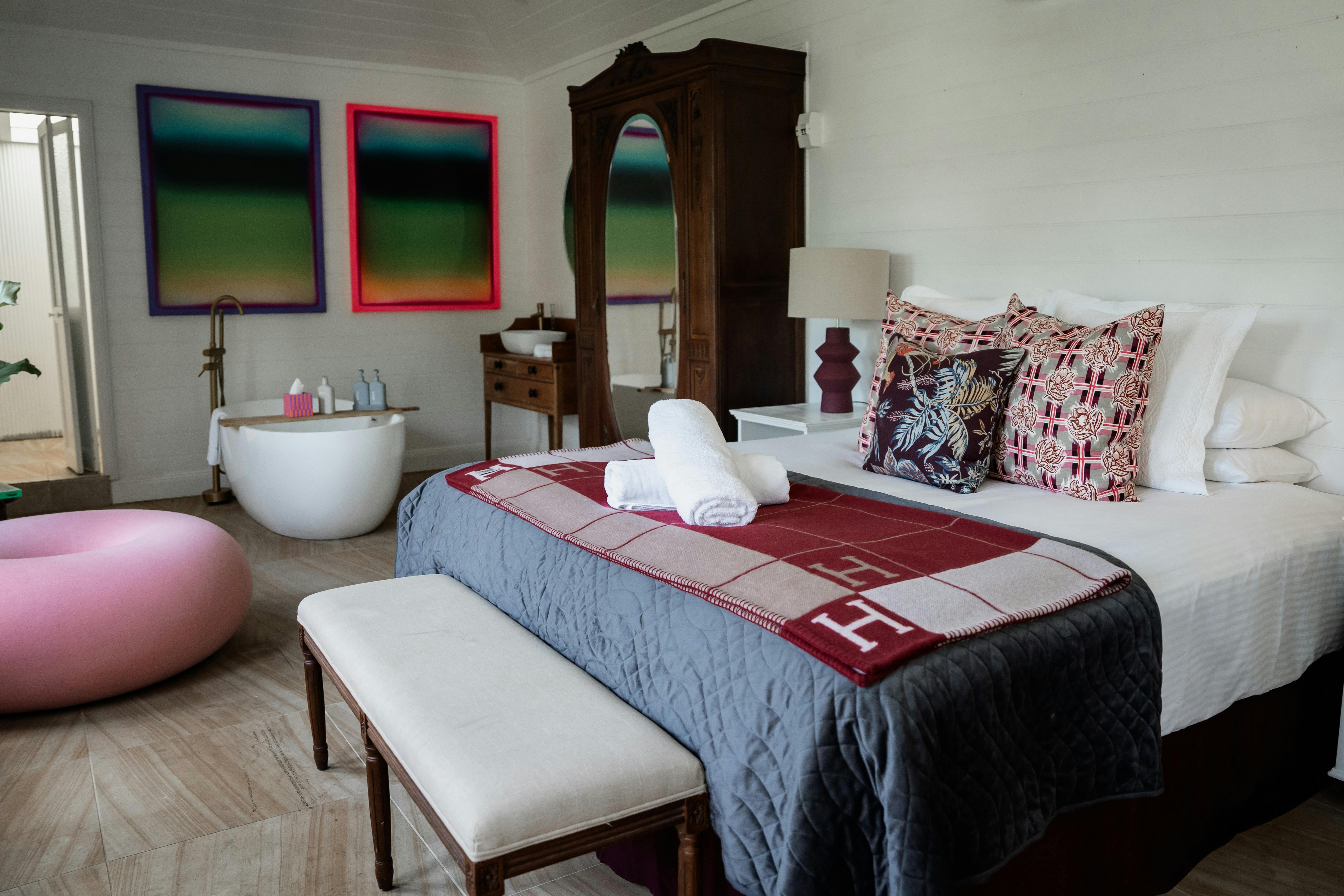 에르메스 담요가 놓인 킹 사이즈 침대 배경에 욕조가 있고 다채로운 예술 작품이 있습니다.