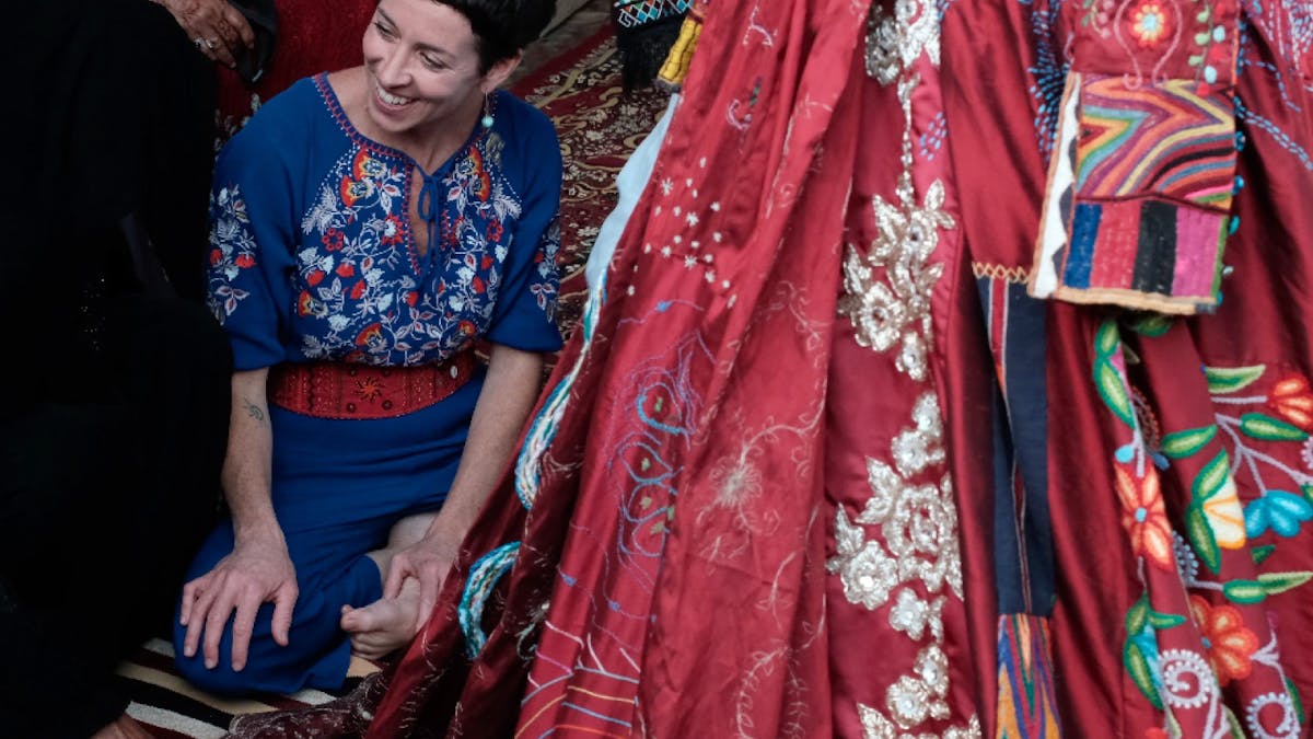 A smiling woman sitting on the ground next the an embroidered red skirt