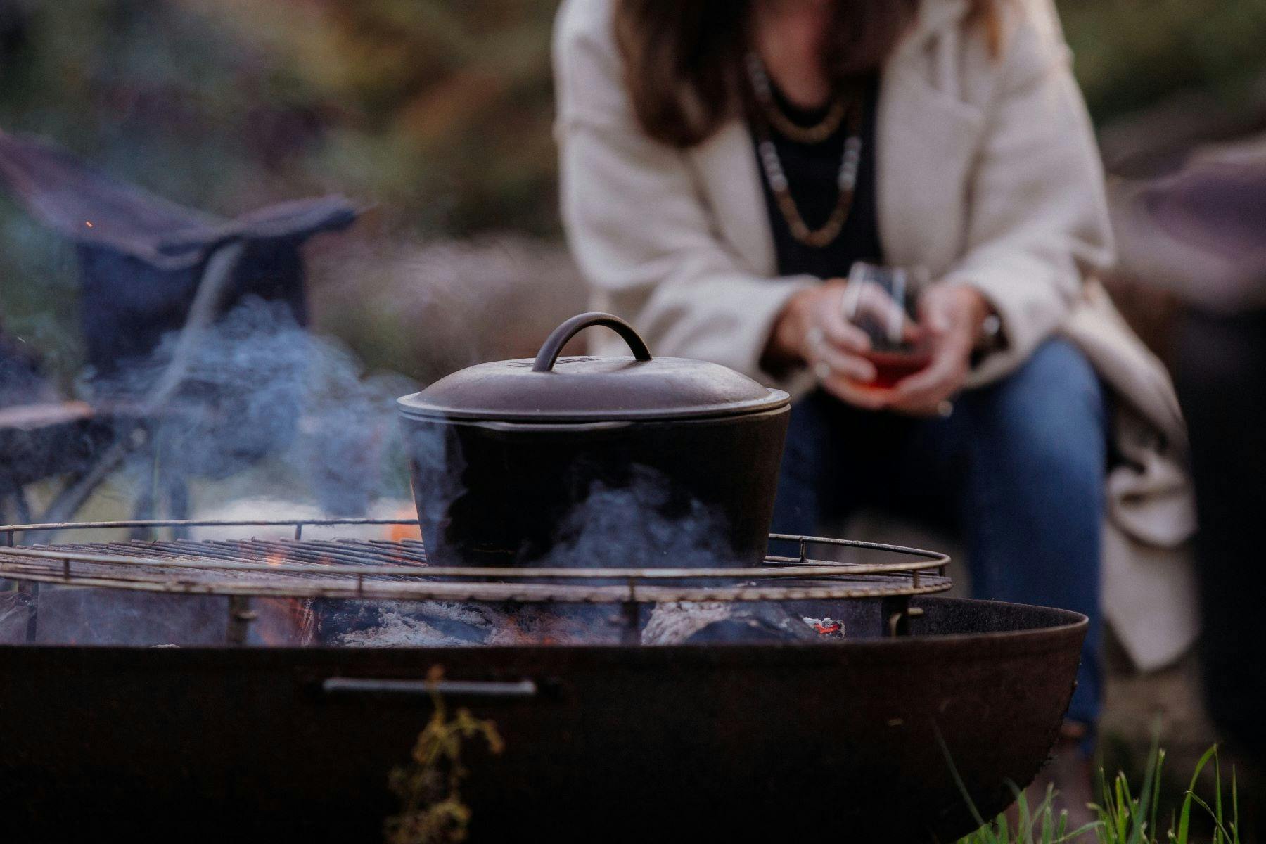 Cast iron pot sitting on grill over fire pit with woman in background
