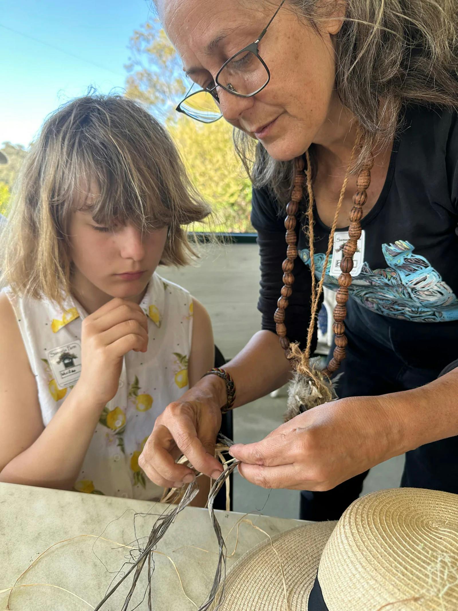 Older women teaching a young child how to basket weave