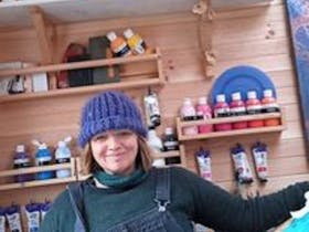 A photo of Selena Smith a talented artist, wearing a blue knitted hat blue, overalls and green top.