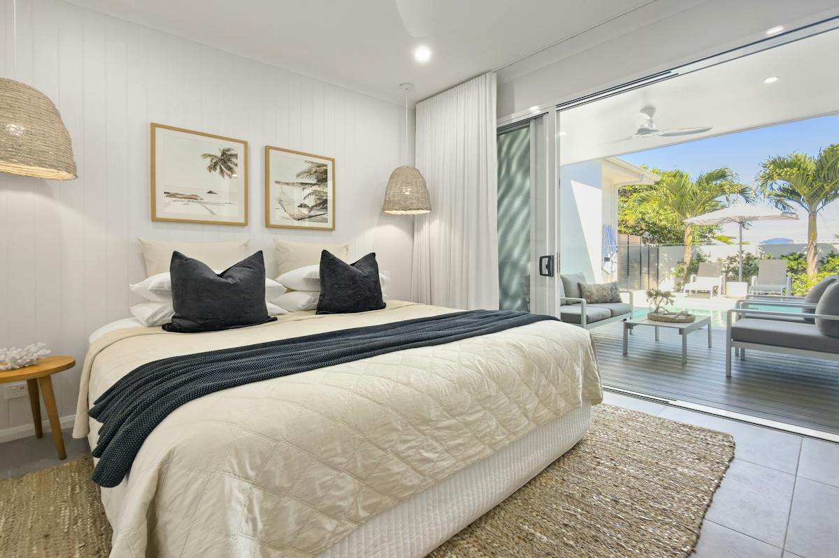 Coastal style bedroom flowing out to patio and pool with palm trees in background