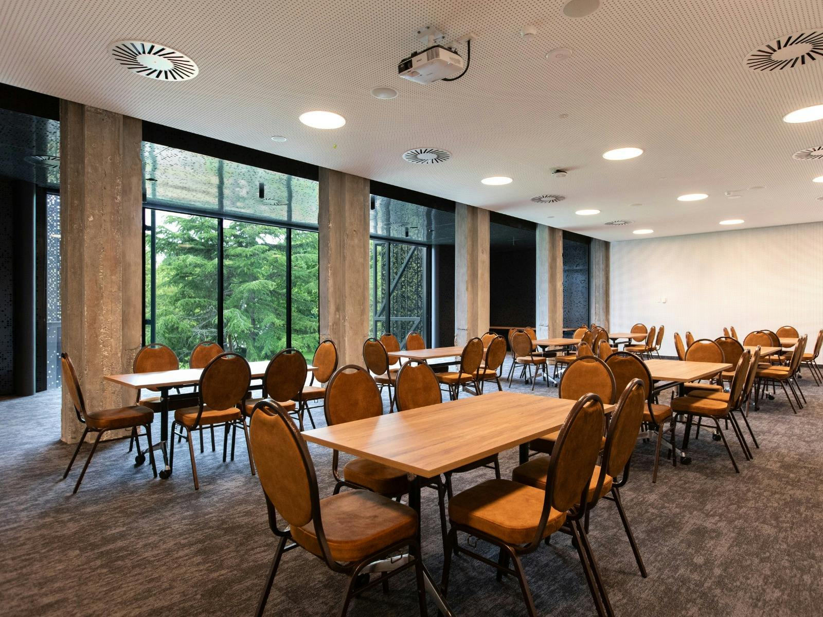 A large conference room with white walls, chairs and tables, and a view out to a park